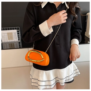 Detail view of a bright orange oval crossbody bag with a large gold metal arc ornament
