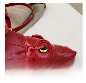 Close-up of red crocodile-shaped bag head featuring yellow eyes and textured faux leather