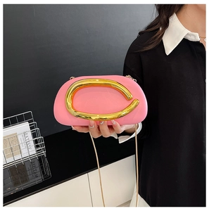 Detail of pink elliptical crossbody bag with gold C-shaped handle and chain strap