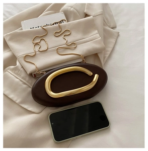 Detail of a dark brown mini evening bag with a gold metal handle and a snake chain strap