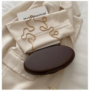 Detail of a dark brown oval evening bag with a gold snake chain on a beige blazer