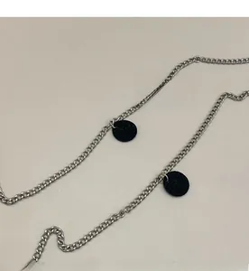 Detail of a sleek silver metal long chain strap with two black litchi leather round pendants