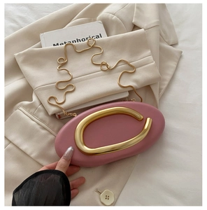 Detailed view of pink oval evening bag with gold metal handle and chain on a beige blazer