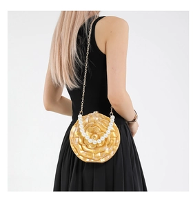 Macro detail of camellia evening bag with golden metallic finish and pearl handle