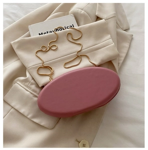 Pink oval evening clutch bag with golden chain strap on stylish beige suit and fabric