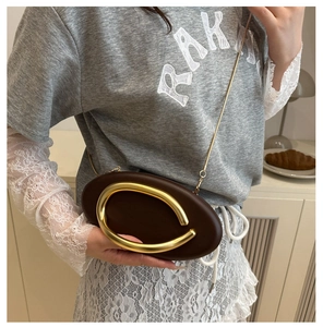 Detail of dark brown leather oval clutch with irregular gold metal handle and chain