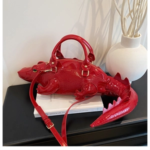 Detail of red crocodile-shaped handbag with glossy finish and golden metal hardware