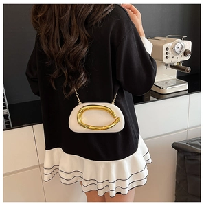 Close-up of modern ivory crossbody bag featuring a large decorative gold metal ring