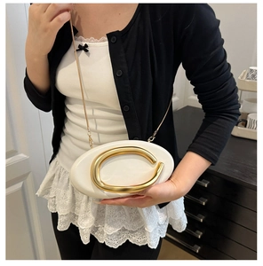 White oval clutch bag with gold C-handle and chain strap worn by a model