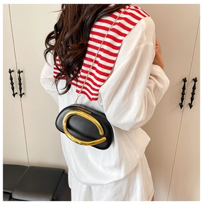 Model wearing a black leather oval bag with a large gold C-shaped metal buckle and chain