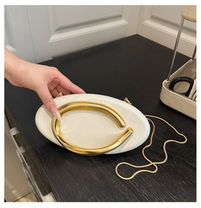 Detail of white oval clutch bag featuring a gold C-shaped metal handle and chain strap