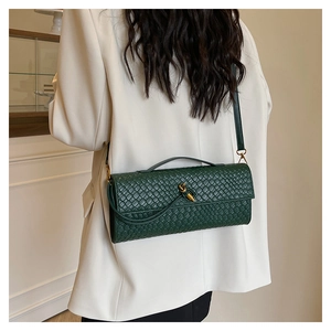 Détail du sac bandoulière tissé vert foncé avec fermoir nœud doré sur blazer blanc