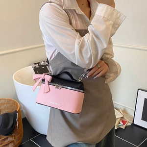 Pink and black cylinder crossbody bag with bow detail and chain strap worn by a model