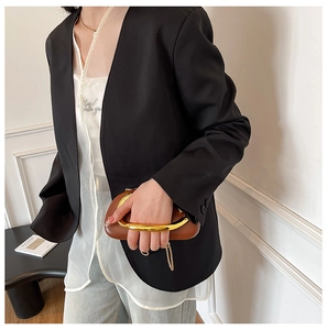 Detailed view of a brown clutch bag with a sculptural gold metal handle and chain strap