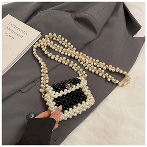 Detail of woven pearl mini bag with camellia floral clasp on dark suit background