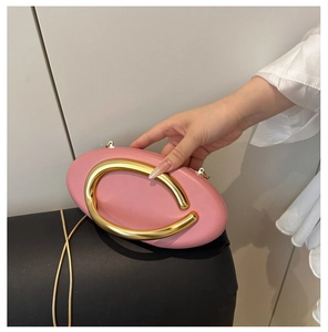 Detail of pink oval clutch bag featuring a large gold metal handle and chain strap
