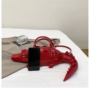 Detail of red crocodile-shaped handbag with realistic scales, dual handles and thin strap