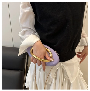 Detailed view of a purple oval clutch bag with a thick gold U-shaped metal handle and chain