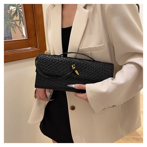 Détail d'un sac bandoulière tissé noir avec boucle dorée sur une veste de costume beige