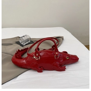 Macro detail of red crocodile shaped bag showing textured faux leather and gold hardware