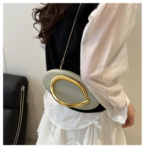 Detail of grey-green oval clutch bag with gold handle and chain on model