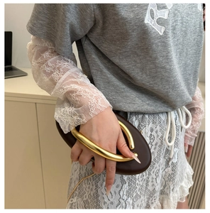 Detail of a dark brown oval evening clutch with a polished gold U-shaped metal handle