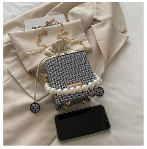 Detail of compact bucket bag with pearl handle and chain next to a smartphone