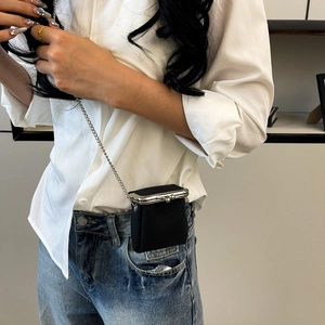 Close-up of a mini black lychee leather lipstick bag with silver chain on model