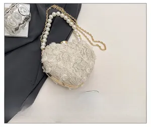 Detail of heart-shaped lace evening bag with pearl handle and gold metal trim