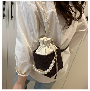 Detail of dark brown woven bucket bag featuring large pearl handle and chain strap