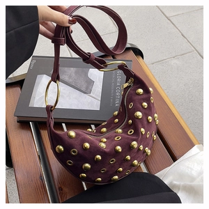 Detail of burgundy suede crescent bag featuring golden rivets and eyelet studs texture