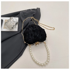 Detail of heart-shaped evening bag with lace texture, pearl handle, and gold chain strap
