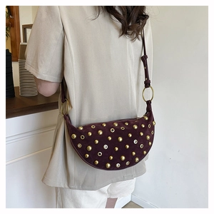 Detailed close-up of a burgundy suede crossbody bag with gold punk studs and eyelets
