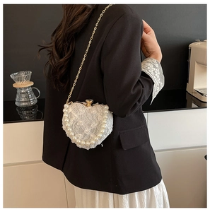 Detail of heart-shaped lace evening bag featuring large pearl trim and gold chain strap