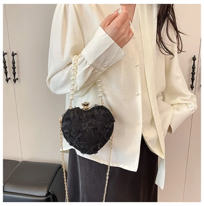 Detail of heart-shaped lace evening bag with pearl handle and golden chain strap