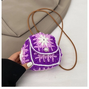 Detail of a handmade purple knit mini bag featuring flower patterns and a pearl button