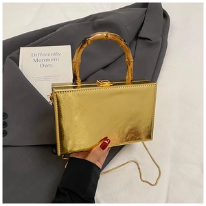 Detail of glossy gold box bag featuring a natural bamboo handle and metal chain strap