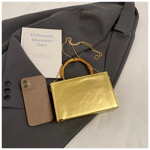 Close-up of metallic gold box bag featuring a bamboo handle and gold chain strap