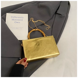 Detailed macro of gold metallic box bag featuring bamboo handle and golden chain strap