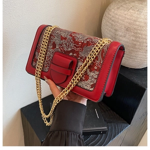 Detail of red embroidered shoulder bag featuring traditional patterns and gold chain strap