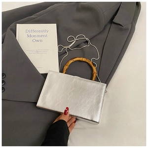 Silver rectangle box bag with bamboo handle and chain strap on a gray blazer