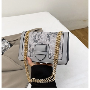Detail of grey crossbody bag featuring floral embroidery and bold gold chain strap