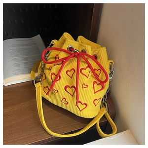 Close-up of yellow corduroy bucket bag with red heart embroidery on wooden table