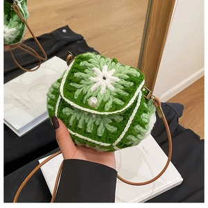 Detail of green knitted crossbody bag featuring floral motifs and a pearl clasp