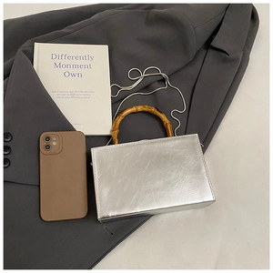 Flat lay of silver glossy box bag with bamboo handle and metal chain on a grey suit
