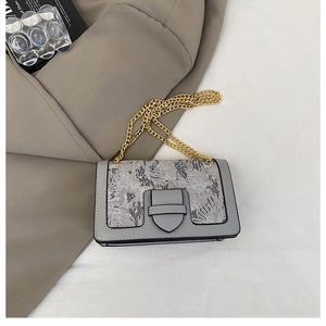 Detailed view of grey crossbody bag featuring intricate floral embroidery and gold chain