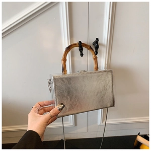 Macro detail of silver rectangular box bag with bamboo handle and metallic texture