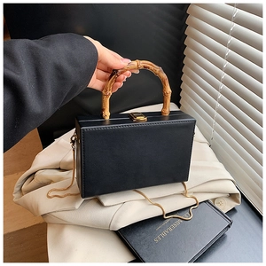 Detail of black box bag featuring natural bamboo handle and gold chain strap