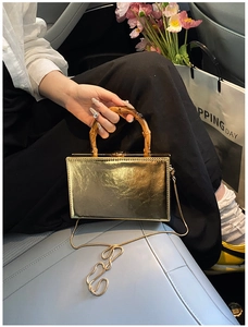 Detail of a gold box bag with a bamboo-style handle and a metallic clasp closure