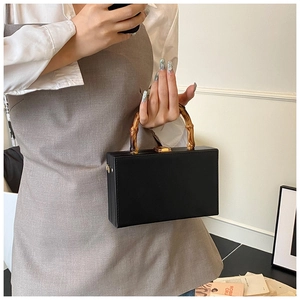 Detailed close-up of a black leather box bag featuring a natural bamboo top handle design